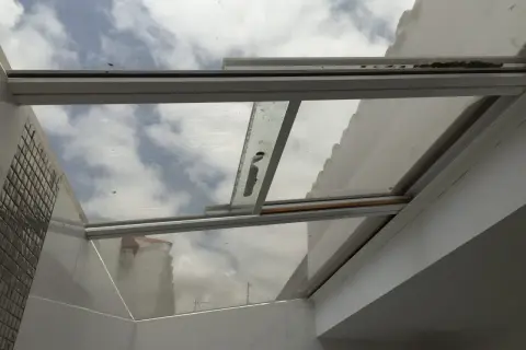 Techos de cristal inconvenientes: suciedad y óxido en los marcos, reflejando un cielo nublado y edificios.