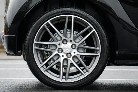 Błyszczące, czarne nadkole samochodu z felgą Brabus i oponą na mokrej nawierzchni.