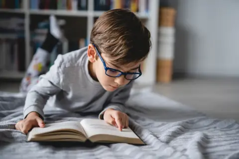Niño con gafas azules concentrado en un libro abierto, aprendiendo a leer.