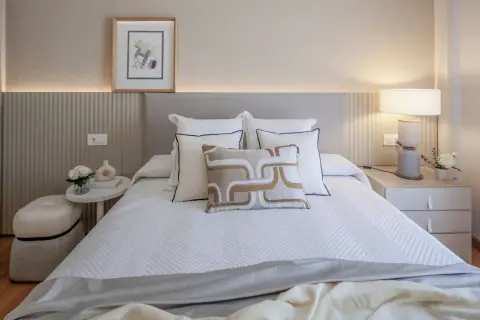 Elegantes ideas de habitaciones de matrimonio con cama blanca, cojines decorativos y mesita de noche con lámpara.