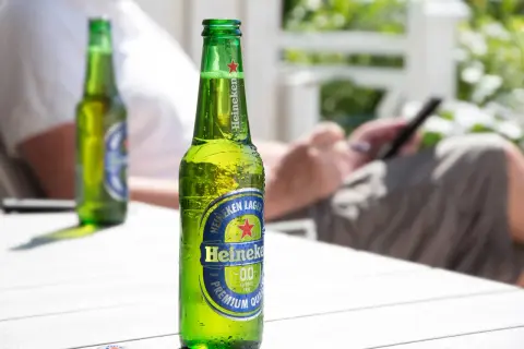 Orzeźwiające piwo bez cukru Heineken 0.0 na stole, w tle osoba korzystająca z telefonu.