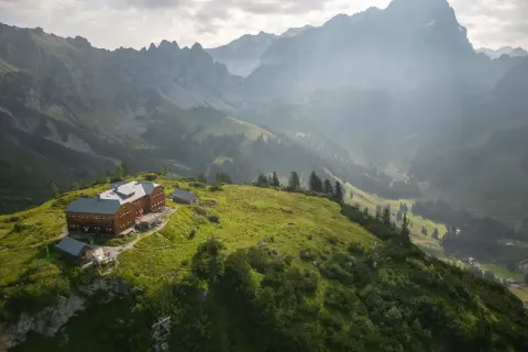 Holzhaus auf einem grünen Hügel, umgeben von majestätischen Bergen. Ein perfekter Ort für die Dachstein Sonnenrunde.