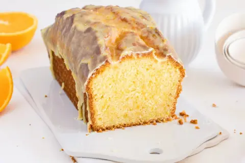 Bizcocho de naranja y chocolate cubierto con glaseado, con rodajas de naranja al lado.