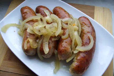 Biała kiełbasa pieczona w cebuli i musztardzie, podana na białym talerzu.