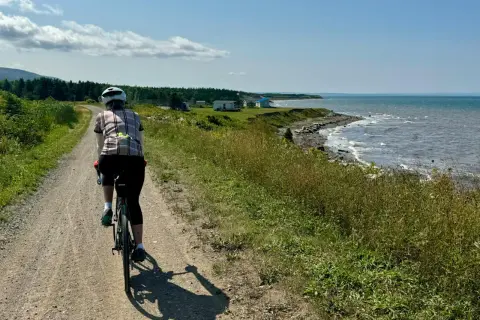 Rowerzystka na leśnych trasach rowerowych, podziwiająca widok na morze i domki na wybrzeżu.