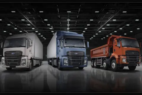 Trois camions Ford F-Line : un blanc avec remorque, un bleu avec remorque, et un orange benne basculante, alignés dans un entrepôt.