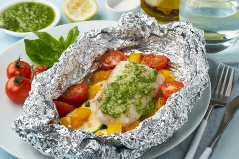 Un délicieux poisson en papillote, garni de légumes colorés et d'une sauce verte savoureuse, prêt à être dégusté.