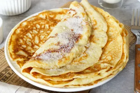 Ein Stapel goldbrauner Pfannkuchen, bestreut mit Zucker. Ein einfaches Pfannkuchen Rezept für jeden Tag.