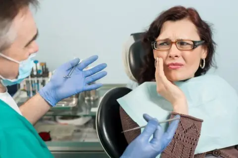 Dentysta wyjaśnia pacjentce, na czym polega zatrucie zęba, która odczuwa silny ból.