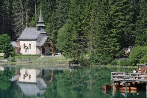Suggestiva chiesa nel lago trentino, con riflessi sull'acqua verde smeraldo e un pontile in legno con barche.