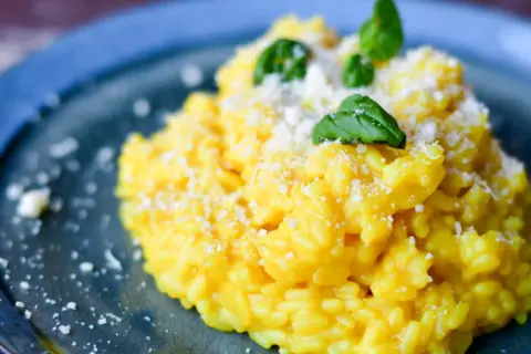 Pyszny, kremowy ryż do risotto, posypany parmezanem i udekorowany listkami bazylii, na niebieskim talerzu.