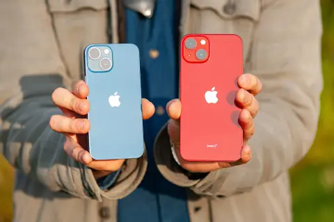 Dwie ręce trzymają dwa telefony: niebieski i czerwony iPhone 13 mini. Oba mają charakterystyczny aparat.
