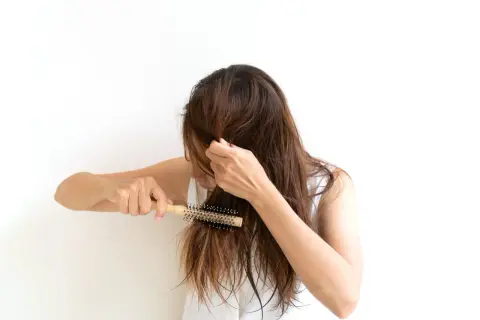 Mujer con cabello castaño se peina con un cepillo redondo, buscando un tratamiento para pelo que se rompe.
