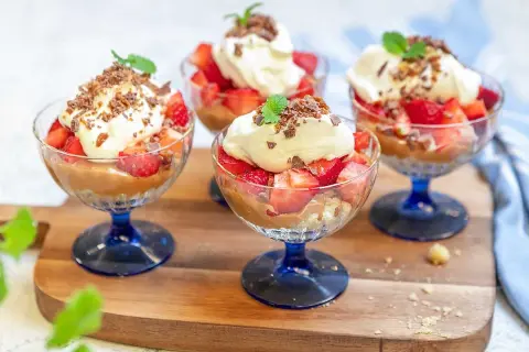 Fyra glas med jordgubbar, grädde och chokladsmulor. En härlig somrig dessert som ser otroligt god ut!
