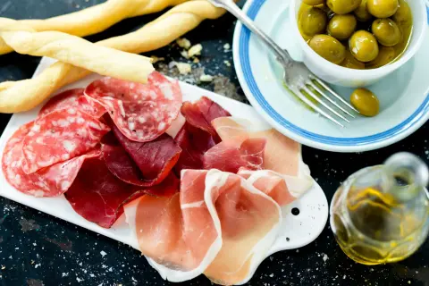 En härlig italiensk tapasbricka med salami, prosciutto, grissini, oliver och olivolja. Perfekt för en mysig kväll.