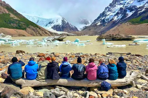 Gruppe sitzt auf Baumstamm vor Gletschersee mit Eisbergen. Tolle Eberhardt Travel Erfahrungen in Patagonien.