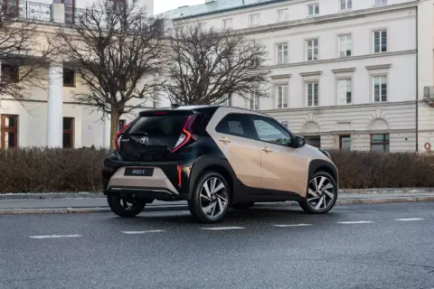 Dwukolorowy Toyota Aygo X na ulicy, z tyłu widoczny budynek z kolumnami.