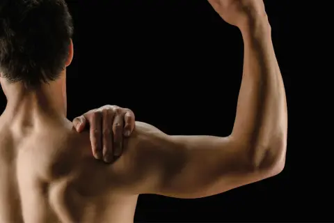 Mężczyzna z ręką na ramieniu, pokazujący umięśnione plecy i biceps. Białko po treningu wspiera regenerację mięśni.