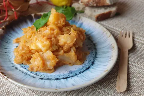 Un plato de col con patatas, guisado y servido con hojas verdes. Acompañado de pan y limón.