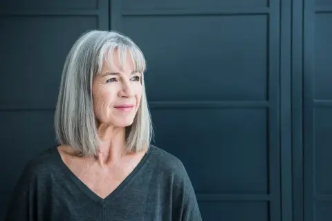 Een vrouw met grijs haar kijkt peinzend weg. Ze straalt een rustige kracht uit, wat kan passen bij de complexiteit van autisme bij vrouwen.