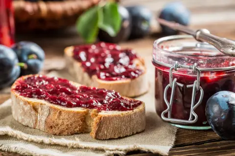 Zwei Scheiben Brot mit Zwetschgenmarmelade mit Zimt, daneben ein Glas der Marmelade und frische Zwetschgen.