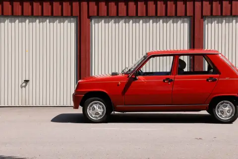 Röd Renault 5 GL står parkerad framför en röd och vit garagebyggnad. Denna klassiska le car är redo för en tur.