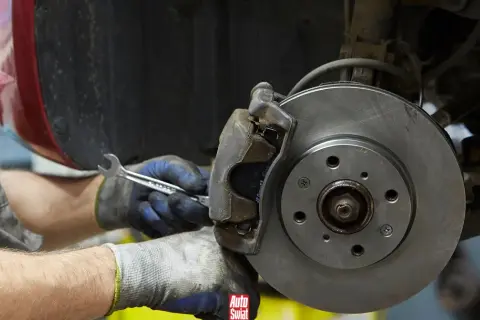 Mechanik w rękawicach dokręca śrubę przy budowie klocka hamulcowego.
