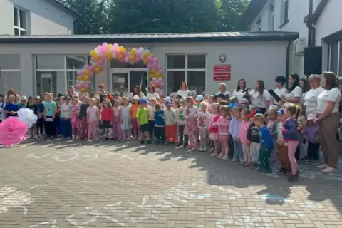 Dzieci i dorośli stoją przed budynkiem ozdobionym balonami. Widać biała podlaska atrakcje dla dzieci, takie jak wielkie papierowe kwiaty i rysunki na chodniku.