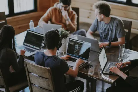 Grupa osób pracuje przy laptopach, dyskutując o regulaminie pracy.
