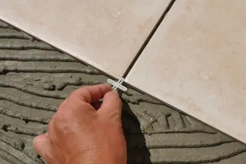 Pose de carrelage en cours, une main place un croisillon. Le prix pose carrelage m2 dépend de la complexité.