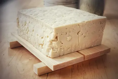 Duży blok domowego, białego tofu na drewnianej podstawce.