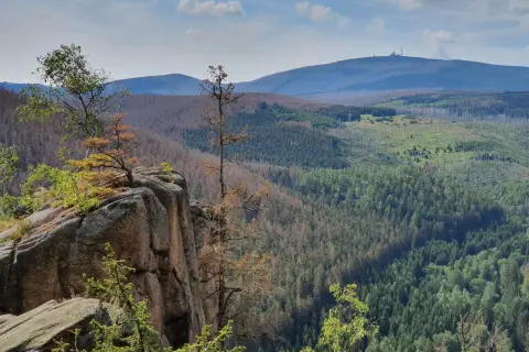 Felsformation an der Rabenklippe im Harz mit Blick auf bewaldete Hügel und den Brocken im Hintergrund.