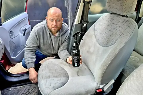 Mężczyzna z butelką środka do czyszczenia skóry w samochodzie, gotowy do odświeżenia wnętrza.