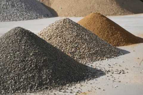 Montones de áridos para hormigón: grava gris oscura, grava clara y arena dorada.
