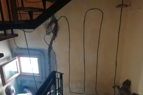 Lavori in corso per l'isolamento pilastri: cavi neri corrono lungo la parete accanto a una scala e una finestra.