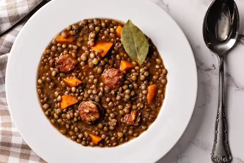 Un plato de lentejas estofadas con trozos de zanahoria y chorizo, decorado con una hoja de laurel.