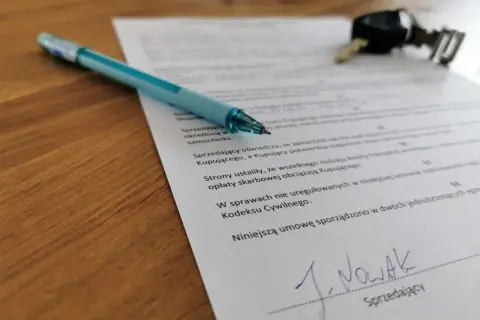 Długopis i kluczyki leżą na dokumencie, który pomoże Ci dowiedzieć się, jak spisać umowę kupna-sprzedaży samochodu.