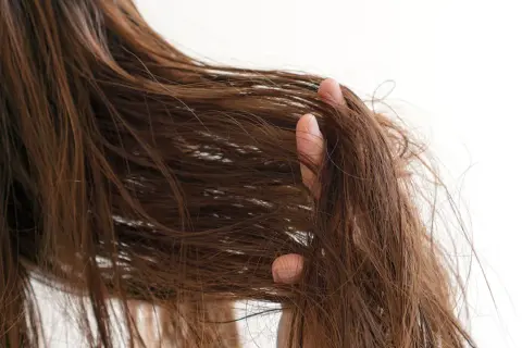 Eine Hand fährt durch braunes, strapaziertes Haar, das trocken und ungepflegt aussieht.