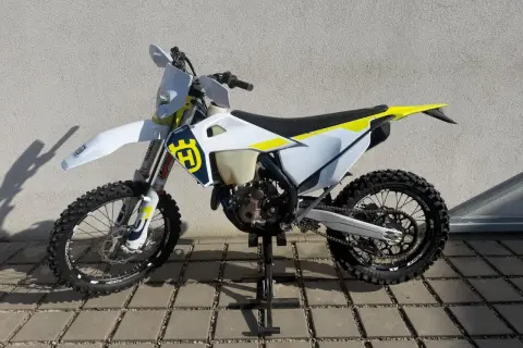 Motocykl Husqvarna WRE 125 na stojaku, biało-żółty, z logo Husqvarna.
