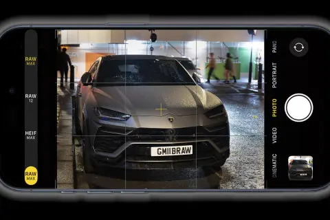 Un'auto sportiva grigia, con targa GMIIBRAW, inquadrata dall'app fotocamera di un iPhone con opzione apple proraw attiva.