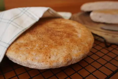Pan de arroz redondo y dorado, cubierto parcialmente con un paño a cuadros, sobre una rejilla.