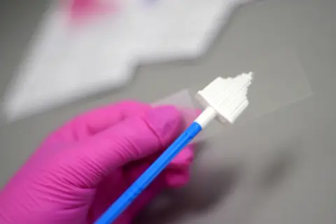 Różowa rękawiczka trzyma szczoteczkę do pobierania wymazu. Przygotowanie do cytologii cienkowarstwowej.
