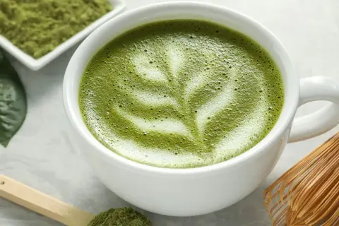 Un délicieux café matcha latte, orné d'une mousse crémeuse et d'une pincée de poudre de matcha sur une cuillère en bois.