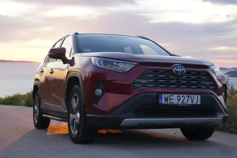 Czerwona Toyota RAV4 2.5 Hybrid na tle zachodzącego słońca nad morzem. Niskie spalanie to jej atut.