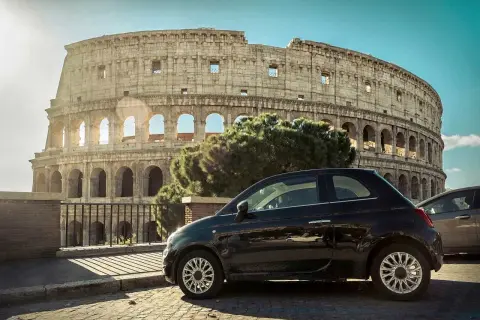 Czarny Fiat 500 zaparkowany przed Koloseum. Idealny sposób na podróż autem do Włoch i zwiedzanie Rzymu.