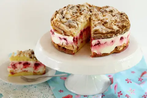 Himmlische Torte mit Baiser, Mandeln und Himbeercreme. Ein Stück ist bereits auf einem Teller angerichtet.