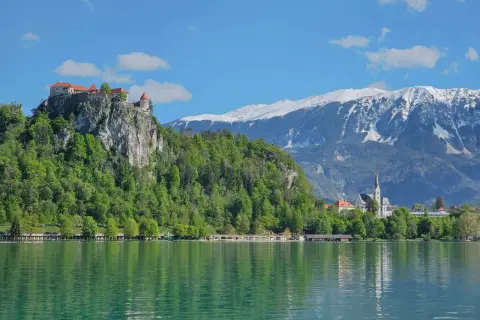 Blick auf die Burg von Bled über dem smaragdgrünen See, mit schneebedeckten Bergen im Hintergrund.