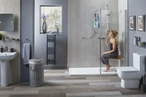 Salle de bain adaptée pour seniors. Une femme utilise une douche avec siège, bénéficiant de l'aide gouvernementale pour une meilleure autonomie.