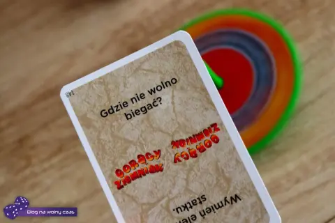Karta z gry "Gorący ziemniak" pyta "Gdzie nie wolno biegać?". W tle kolorowy bączek.