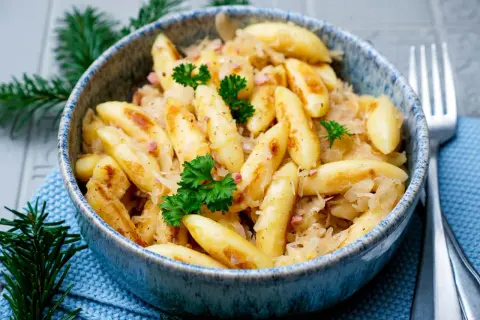 Herzhafte Bubespitzle mit Sauerkraut und Speck, garniert mit Petersilie, in einer blauen Schüssel.